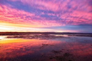 Sunset at Clarks Beach, with reflections in the pools of water on the beach.